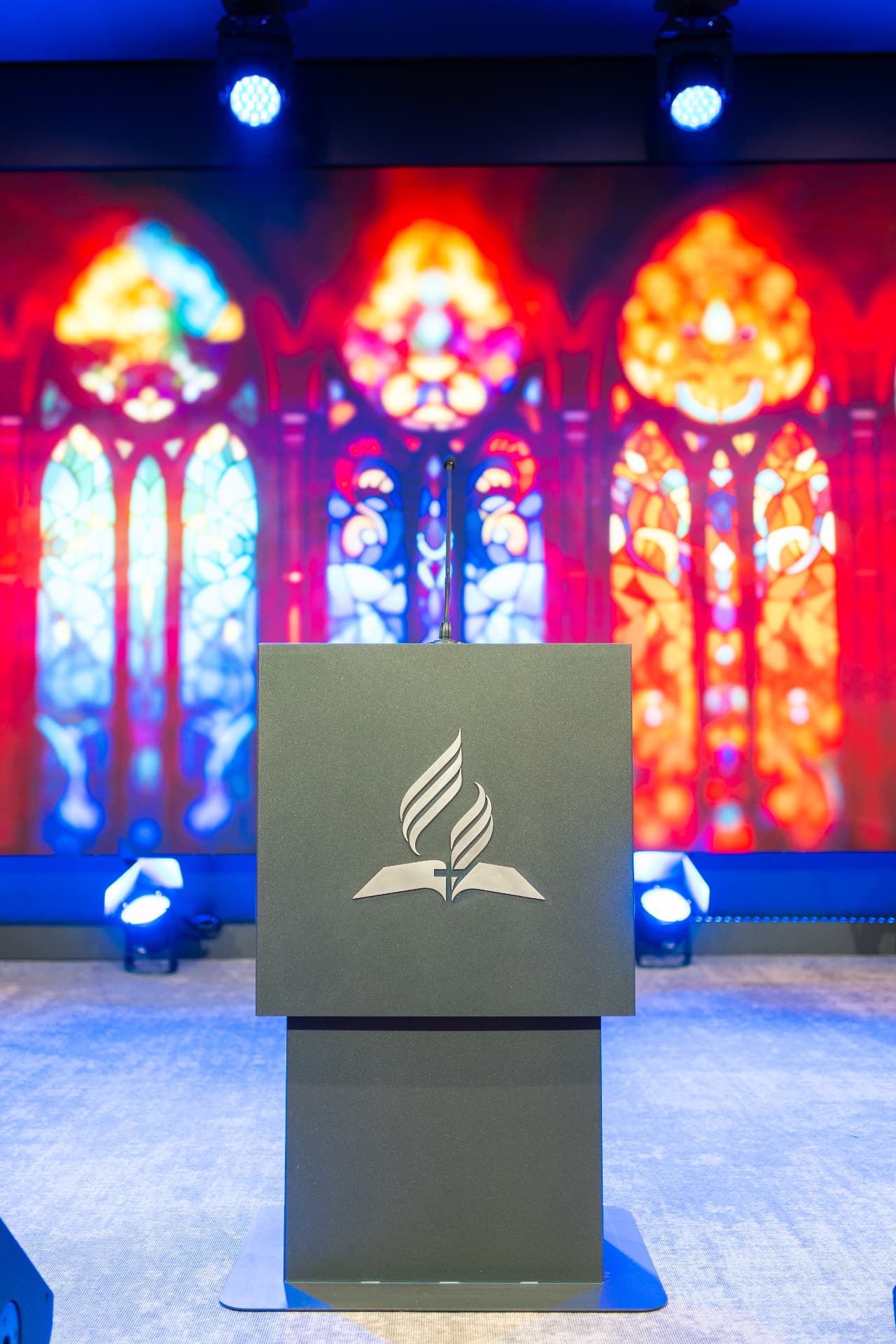 Amvonul cu sigla adventistă în fața unui ecran cu vitralii luminoase, în sala Maranatha